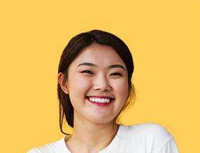 A young asian woman smiling, wearing a white top against a yellow background.