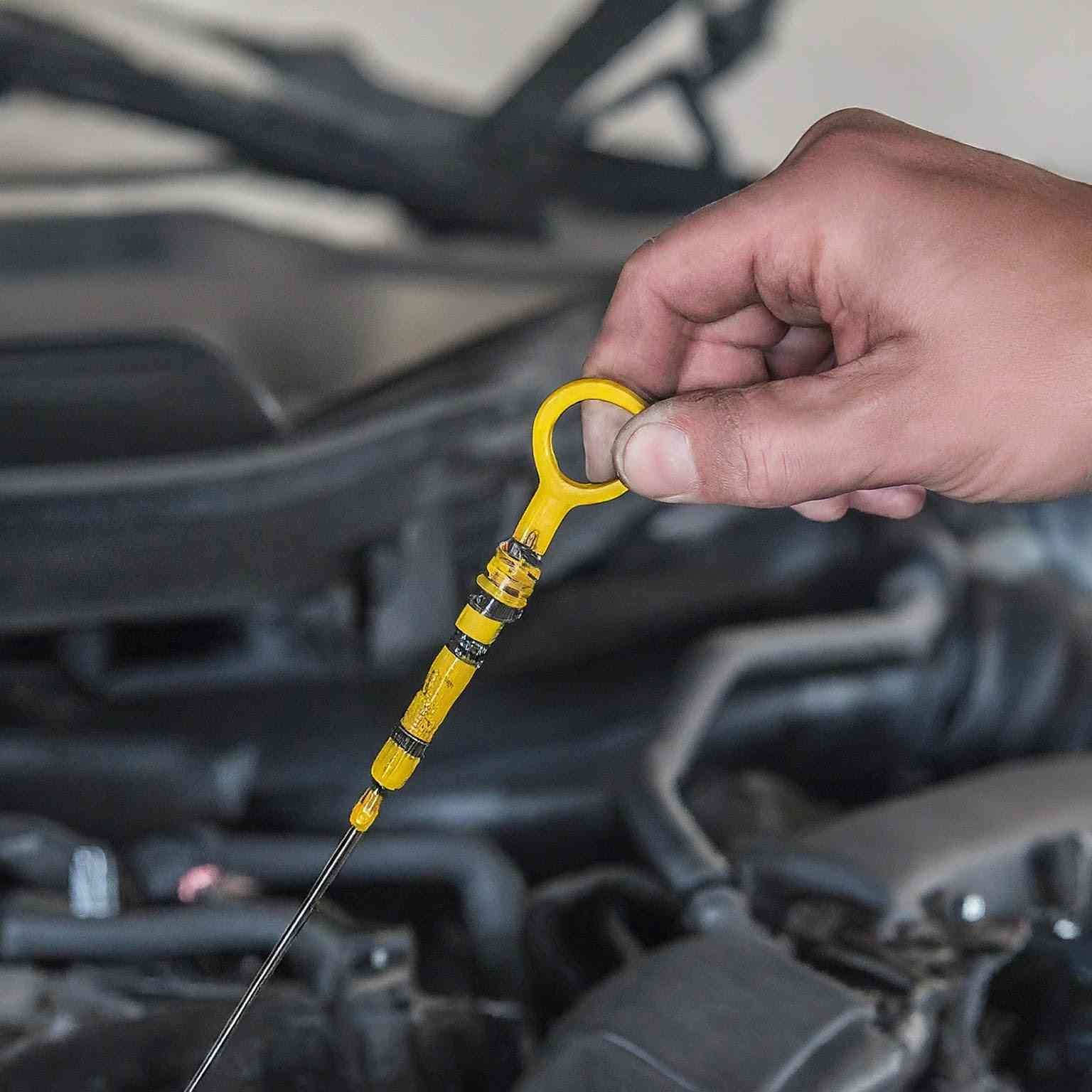 A person's hand holding a yellow dipstick, checking the oil level of a car engine. The background shows engine parts slightly blurred, emphasizing the importance of understanding your car dashboard warning lights.