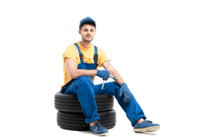 A mechanic in a blue uniform and yellow vest sits on a stack of car tires, holding a wrench, with a thoughtful expression on a green background.