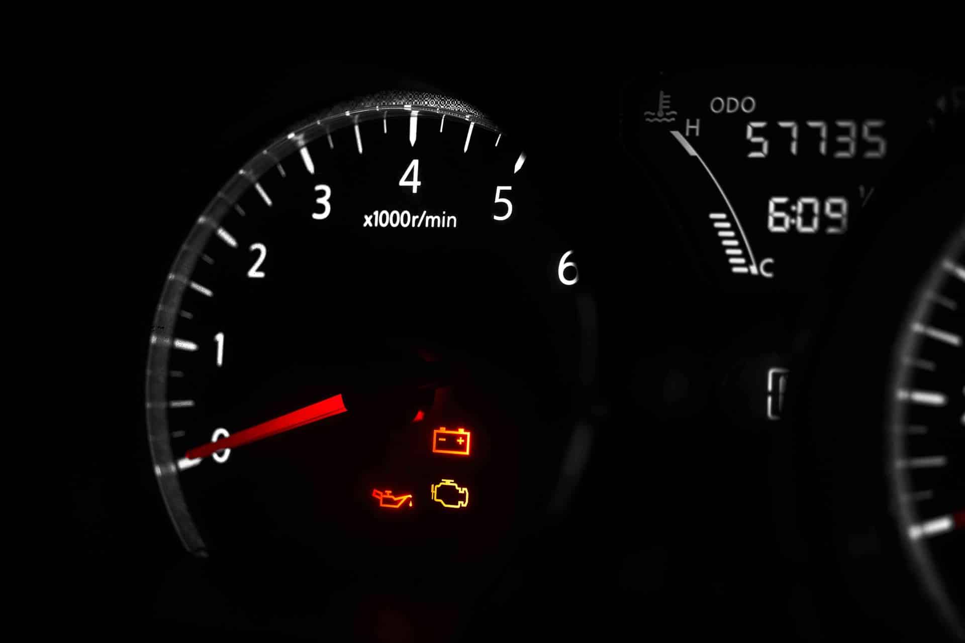 Close-up of a car's dashboard at night, showing a glowing red needle on the tachometer with an engine warning light illuminated. Save up to $60 on wiper blades.